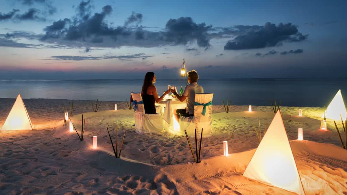 a man and woman at sunset, toasting glasses at a beach side dinner table