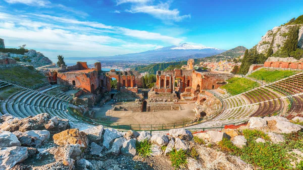 Stone amphitheater of Taormina with the Mediterranean Sea and Mount Etna in the backdrop.